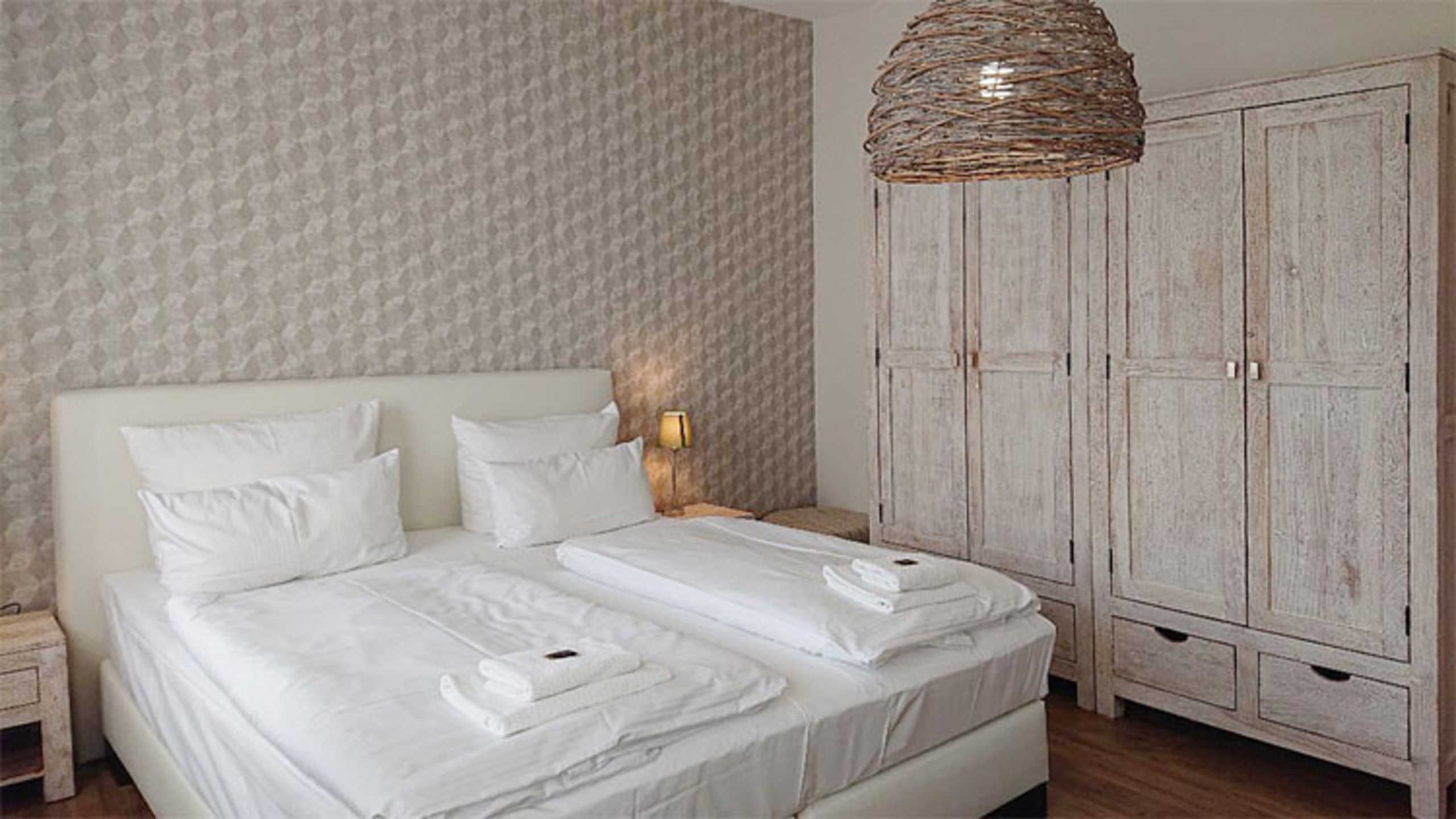 Une chambre à coucher comprenant un lit, deux tables de chevet, une lampe, une armoire et un luminaire suspendu.