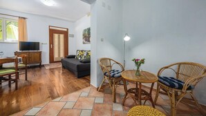 A living room with a sofa, two wicker chairs, a small round table with a vase, a television, and a wooden cabinet. - Beach front apartment in Rabac with WiFi (Rabac)
