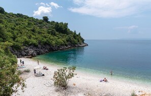 Una playa con agua turquesa cristalina, arena blanca y acantilados rocosos.