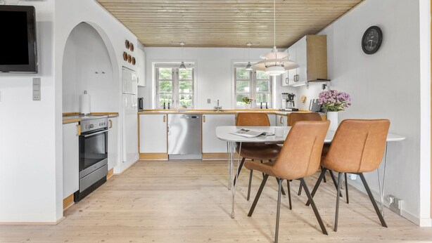 A modern kitchen with white cabinetry, a wooden ceiling, and a dining area with a white table and brown chairs. - 3 bedroom nice home in Brovst (Brovst)