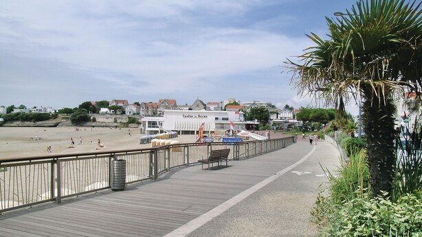 A boardwalk with a casino named 'Casino de Royan' in the background, a sandy beach, and a palm tree on the right.