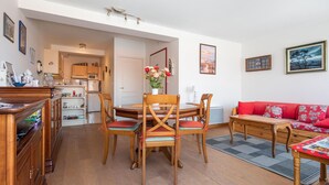 A cozy living room with a dining area, wooden furniture, a red sofa, and a kitchen in the background.