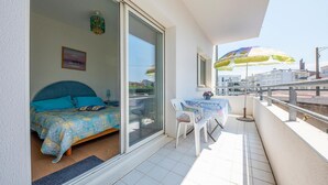 A balcony with a bed, a chair, a table, and a colorful umbrella.
