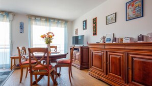 A dining area with wooden chairs and a table, a TV on a cabinet, and various framed pictures on the wall.