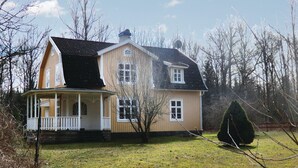 Una casa de dos pisos con un porche, una chimenea y un pequeño jardín.