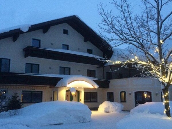 A hotel with a snow-covered entrance, a covered porch, and a tree with lights.