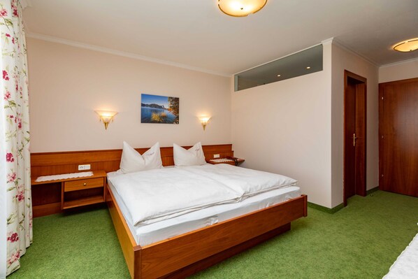 A bedroom with a wooden bed, two bedside tables, a nightstand, a wall-mounted lamp, a painting, and a door.