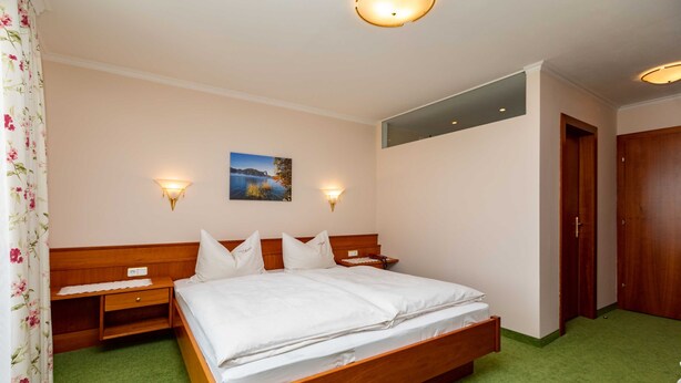 Een slaapkamer met een houten bed, twee nachtkastjes, een wandlamp, een schilderij en een deur.