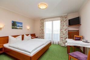 A hotel room with a bed, a desk with a chair, a television, and a window with curtains.
