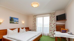 Een hotelkamer met een bed, een bureau met stoel, een televisie en een raam met gordijnen.