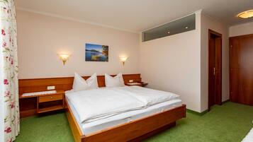 Een slaapkamer met een houten bed, twee nachtkastjes, een wandlamp, een schilderij en een deur.