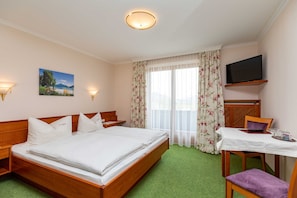 Een hotelkamer met een bed, een bureau met stoel, een televisie en een raam met gordijnen.