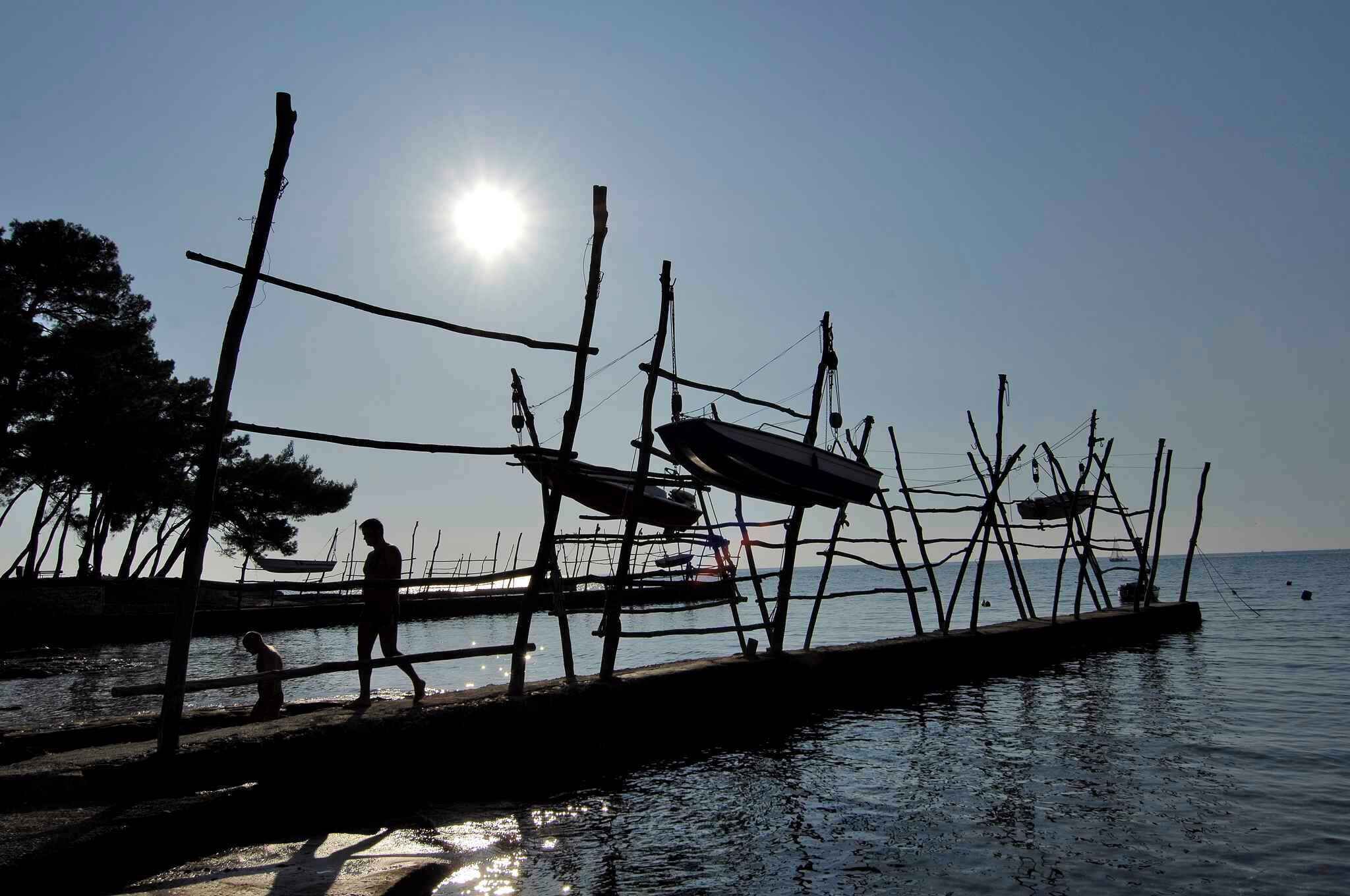 Une jetée dotée d’une simple structure en bois, une personne qui marche et un bateau en arrière-plan.