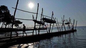 Une jetée dotée d’une simple structure en bois, une personne qui marche et un bateau en arrière-plan.