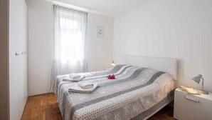 Une chambre bien rangée, avec un lit, une table de chevet, une lampe et une fenêtre avec des rideaux.