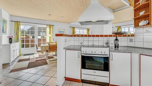 Une cuisine avec un fourneau blanc, une fenêtre et un coin repas comprenant des chaises et une table.
