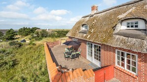 Une maison à toit de chaume dotée d’un patio, d’un mur en briques et offrant une vue sur le paysage environnant.
