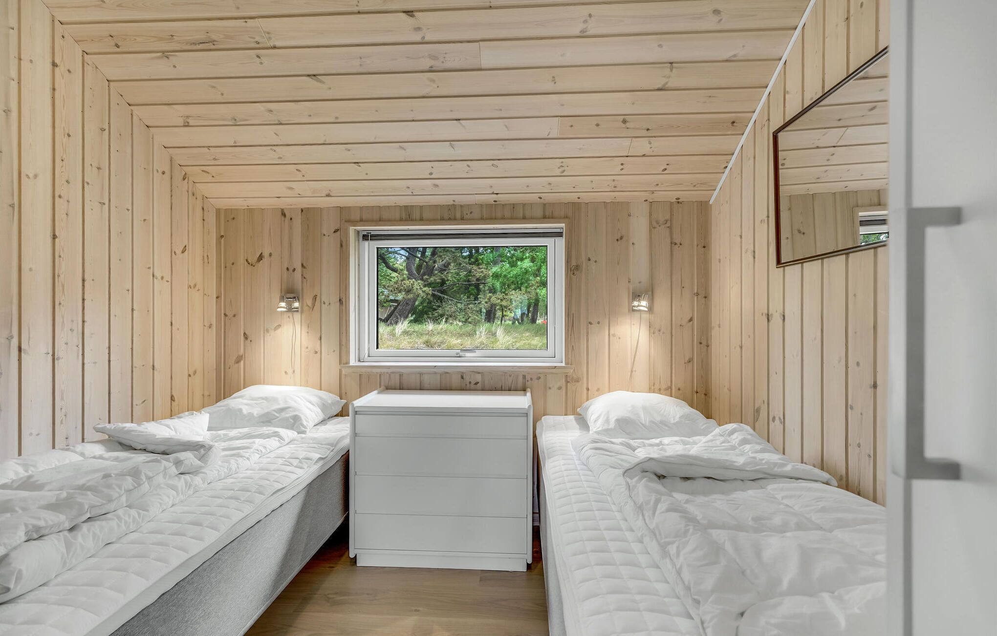 Una piccola stanza in legno con due letti, una finestra e un comò bianco.