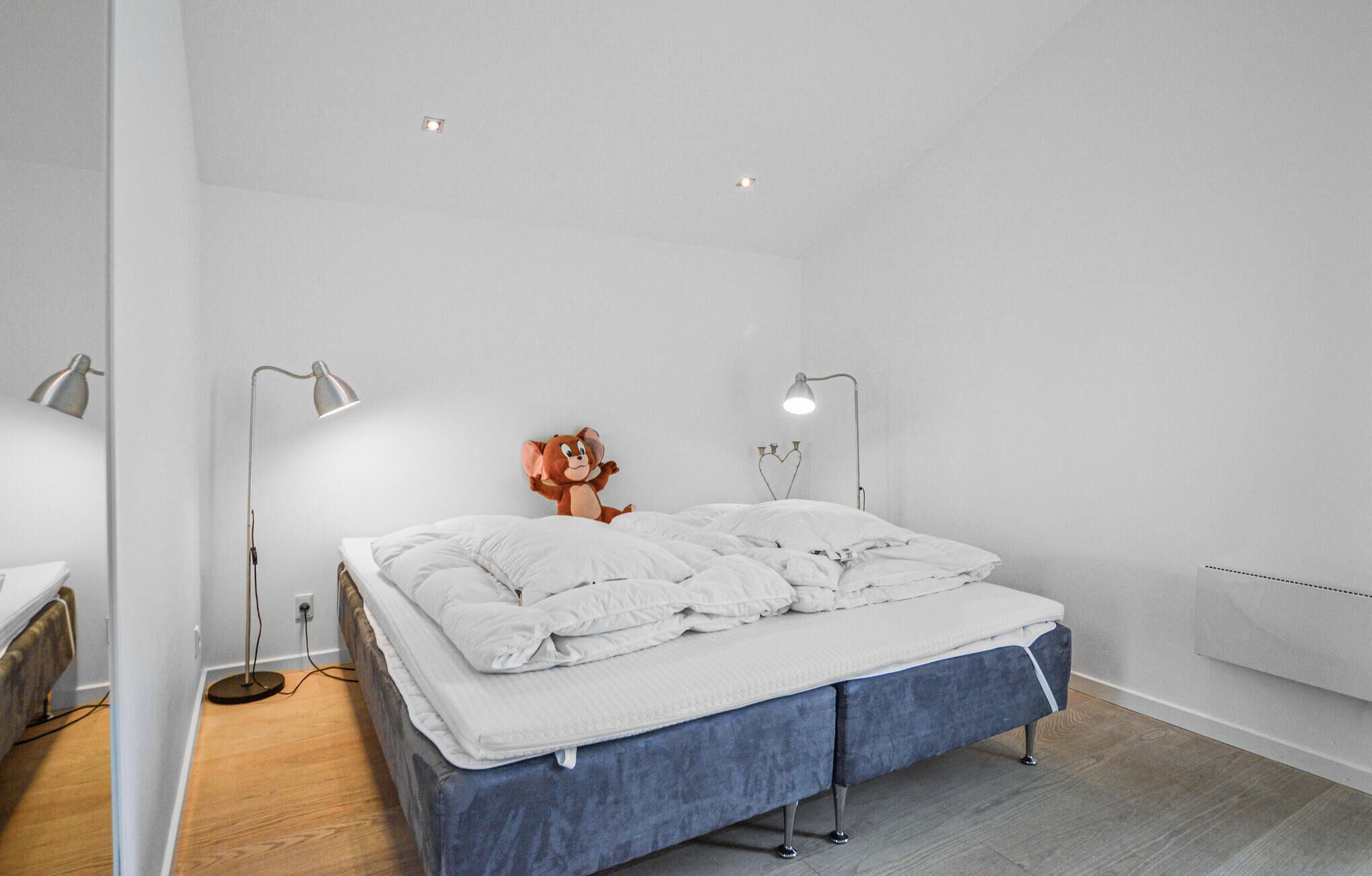 A minimalist bedroom with a bed, two floor lamps, and a wall-mounted radiator.