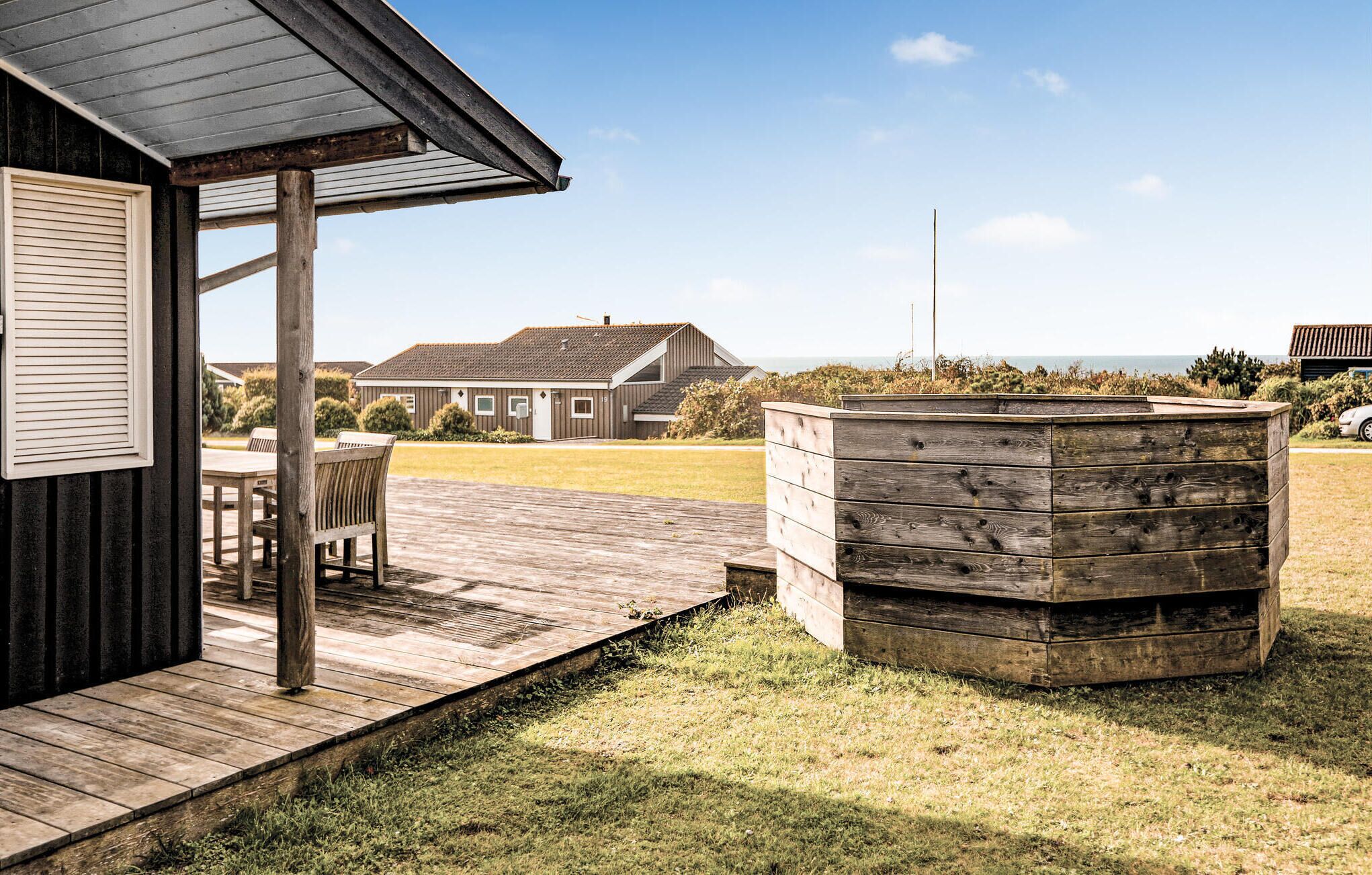 En träaltan med ett bubbelbad, en täckt uteplats och utsikt över ett hus och en strand i bakgrunden.