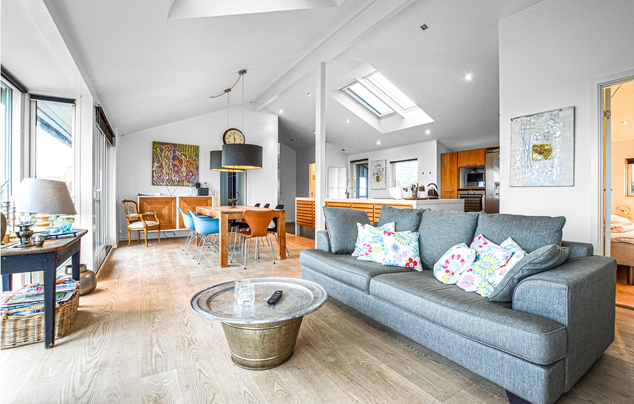 Ein geräumiger Wohnbereich mit grauem Sofa, einem Esstisch und einer Küche im Hintergrund.