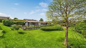 A house with a well-maintained lawn, a wooden deck, and a large tree.
