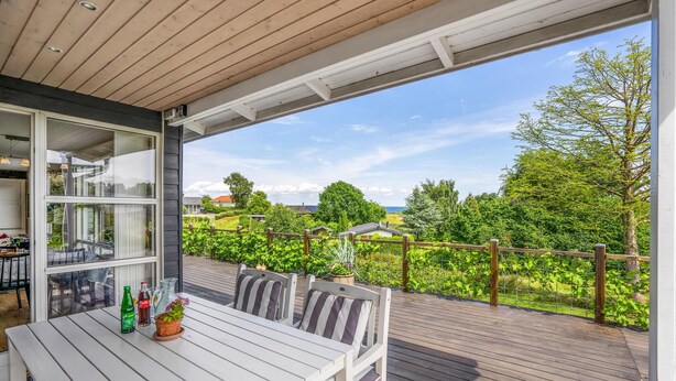 An outdoor deck with a table and chairs, overlooking a lush garden and a distant view of houses.