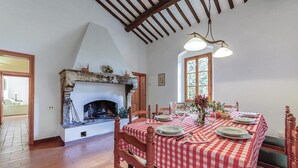 Een eetkamer met een open haard, geruit tafelkleed en houten stoelen.