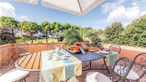 Een buitenruimte met eethoek, een tafel voor vier personen, omringd door metalen stoelen, onder een witte parasol.