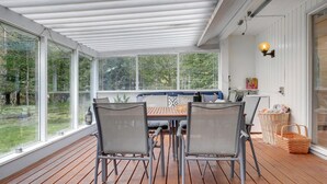 A covered patio with a wooden deck, two grey metal chairs, a wooden table, and a bench with cushions. - Gorgeous home in Aakirkeby with sauna (Aakirkeby)