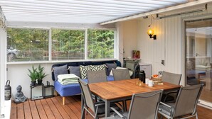 A covered patio with a wooden table and chairs, a blue sofa with cushions, and a Buddha statue. - Gorgeous home in Aakirkeby with sauna (Aakirkeby)