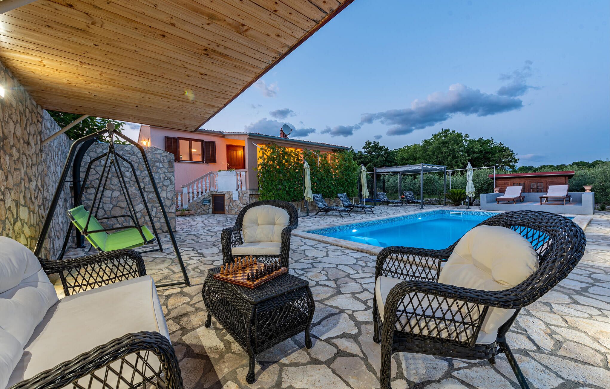 An outdoor pool area with wicker furniture, a swing chair, and a chessboard.