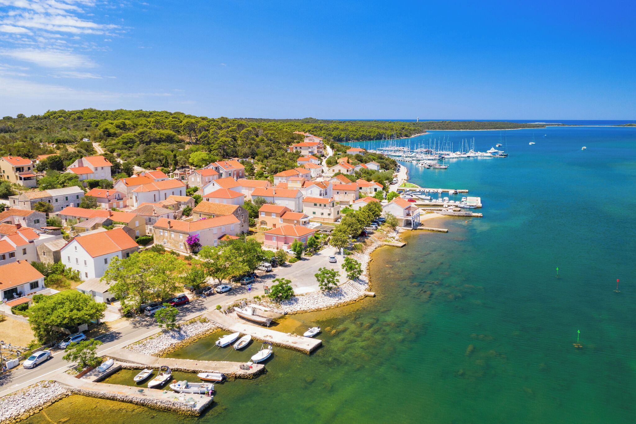 A coastal village with red-roofed houses, a marina, and clear turquoise waters.