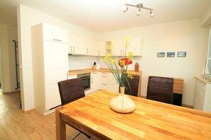 A modern kitchen with white cabinets, a wooden dining table, and a vase with flowers.