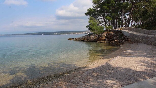 A coastal area with clear water, a pebble beach, and a stone wall with trees. - Studio with balcony and air conditioning (Malinska)