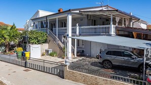 A two-story house with a covered patio, a car parked in the driveway, and a staircase leading to the upper floor. - Studio with balcony and air conditioning (Malinska)