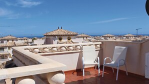 Eine Dachterrasse mit zwei weißen Stühlen, einem Kachelboden und Blick auf das Meer und die Skyline.
