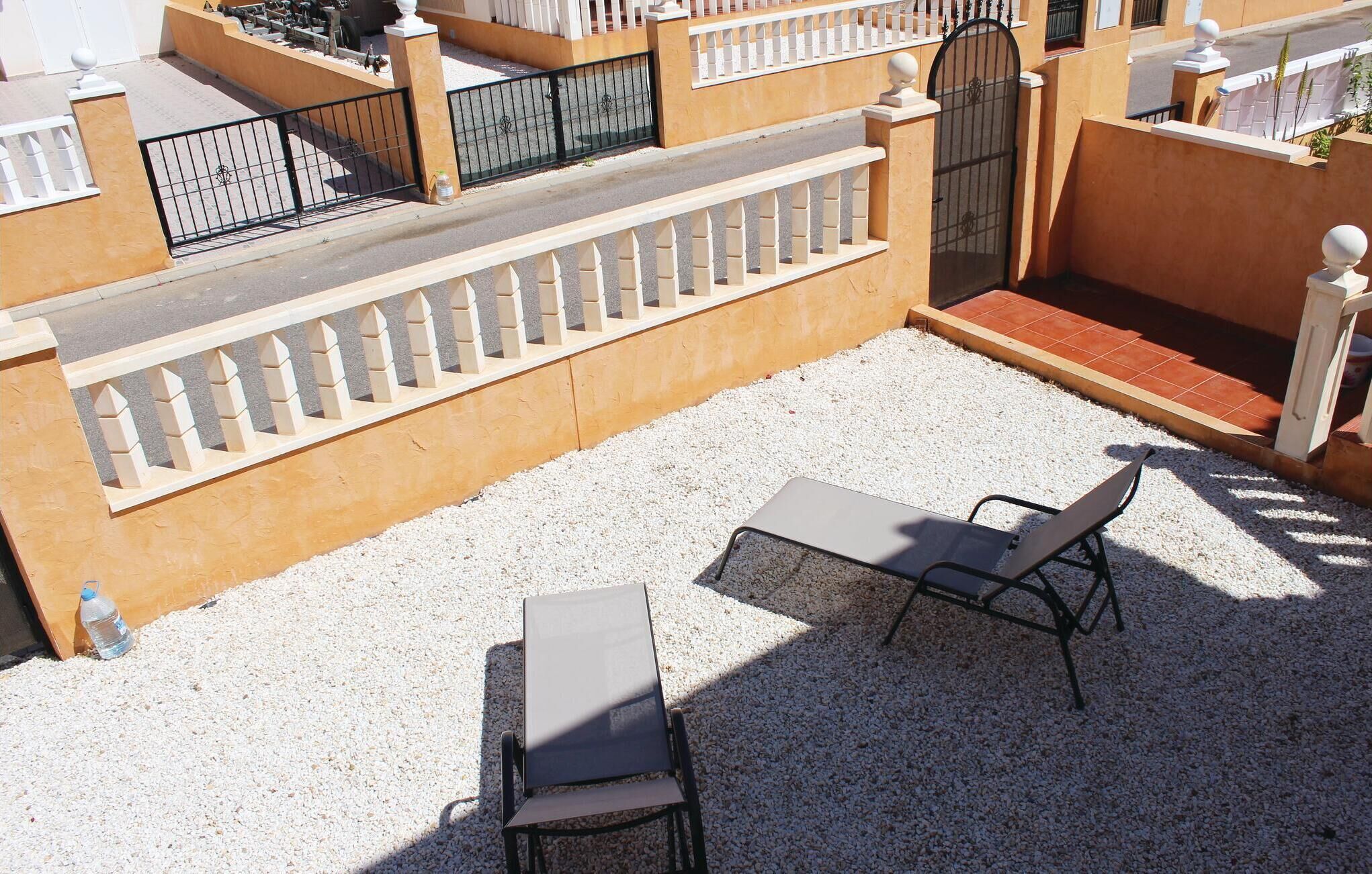 En terrasse med to liggestole og et bord, omgivet af et hvidt hegn og en beige væg.