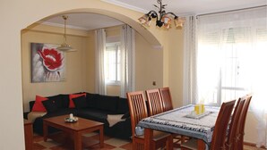 Ein Wohnzimmer mit einer Couch, einem Esstisch mit Stühlen, einem Couchtisch, einem Gemälde und einer Chandelier.