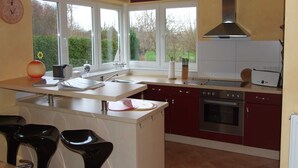 A modern kitchen with a central island, a built-in oven, and a large window providing a view of the outdoors. - Kajüte Vacation Home - - Kajüte Vacation Home - (Brodersby)