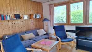 En hyggelig stue med en grå sofa, blå lænestole, et træbord og et tv-bord.