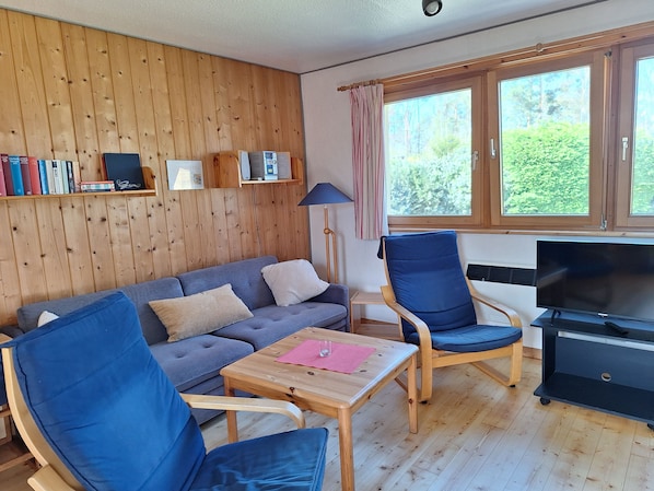 A cozy living room with a grey sofa, blue armchairs, a wooden coffee table, and a TV stand.