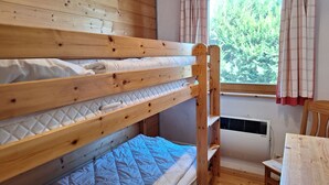 En køjeseng med en quiltet madras, et træhovedgærde og et vindue med gardiner.