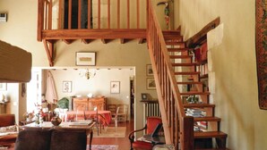 Un vaste salon agrémenté d’un grand escalier en bois, un coin repas avec une table dressée pour quatre personnes, et un espace salon confortable avec un canapé.