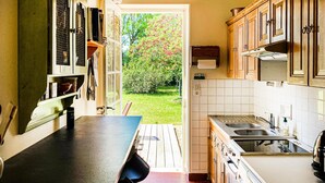 Une cuisine compacte avec un comptoir en bois, un évier et des placards. Une porte donne accès à un jardin verdoyant.