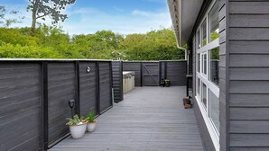 Een overdekt terras buiten met een houten vloer, omringd door donkere houten wanden en een kleine plantenbak met beplanting.