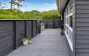 A covered outdoor deck with a wooden floor, surrounded by dark wooden walls, and a small planter with plants.