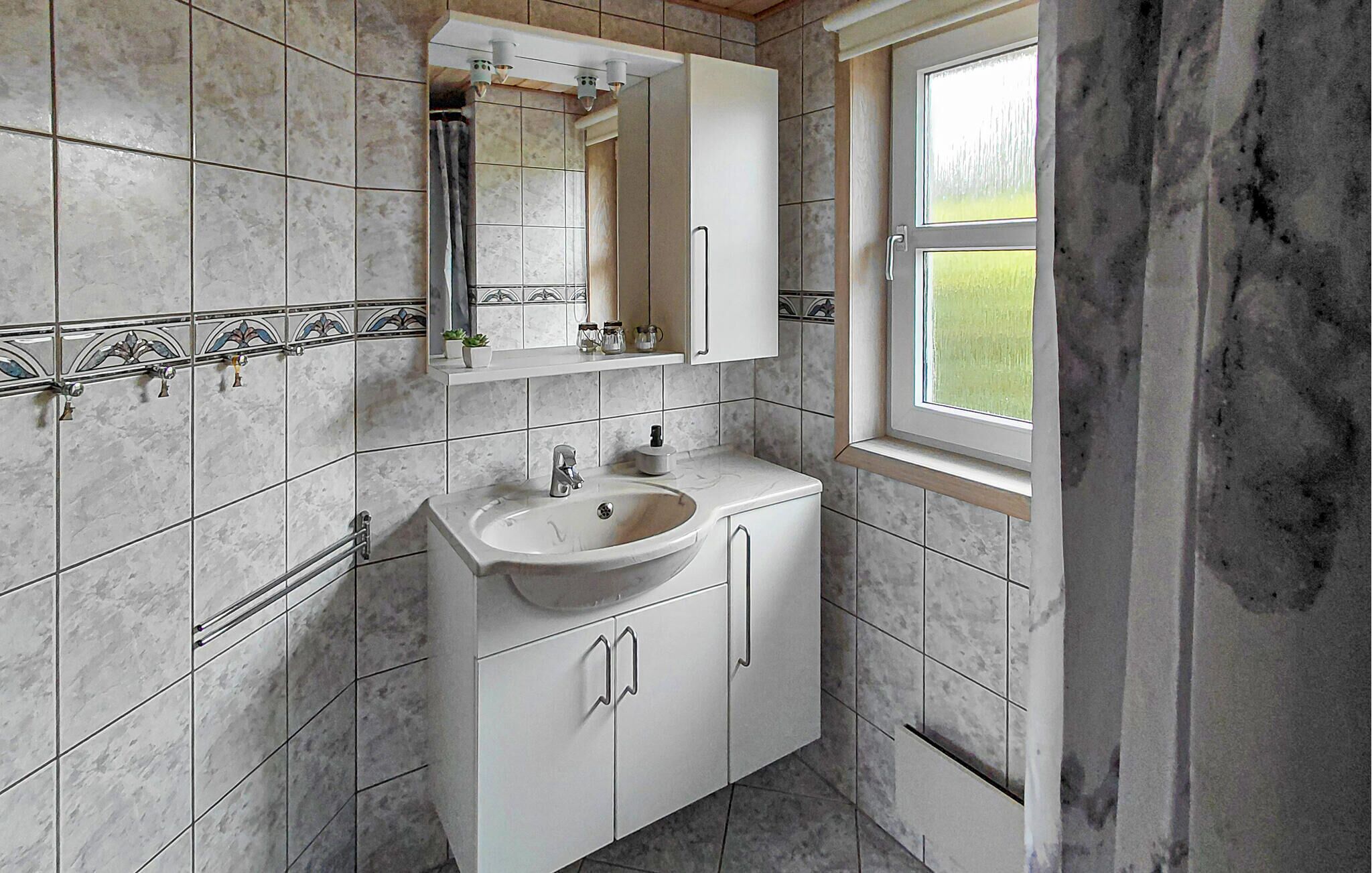 A bathroom with a sink, mirror, cabinets, and a window.