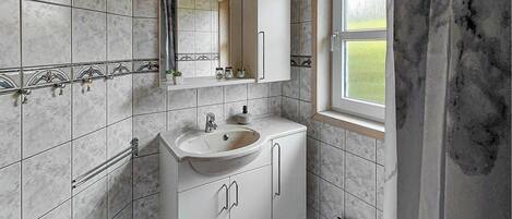 A bathroom with a sink, mirror, cabinets, and a window.