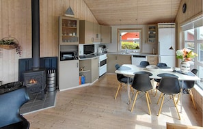 A modern kitchen with a central island, a dining area with a round table and chairs, and a wood-burning stove.